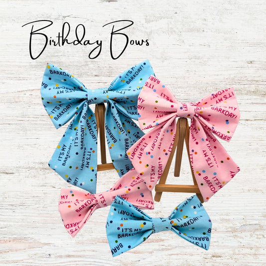 Pink and blue birthday-themed pet bows on a wooden stand with 'Birthday Bows' text above. The bows feature text saying "It's my barkday"