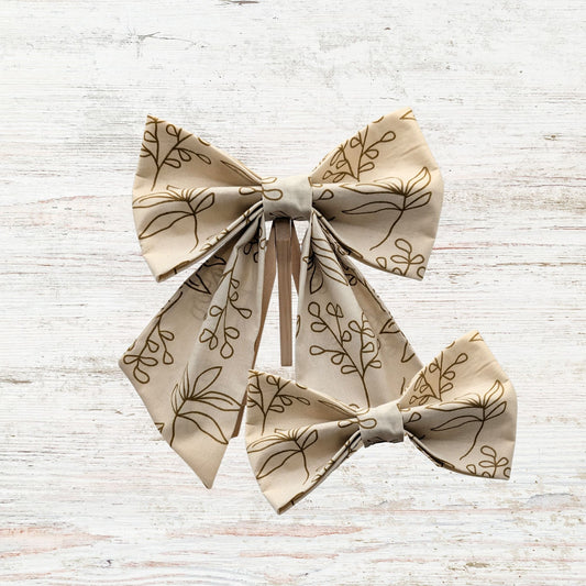 Beige fabric bows with leaf pattern on a light wooden surface