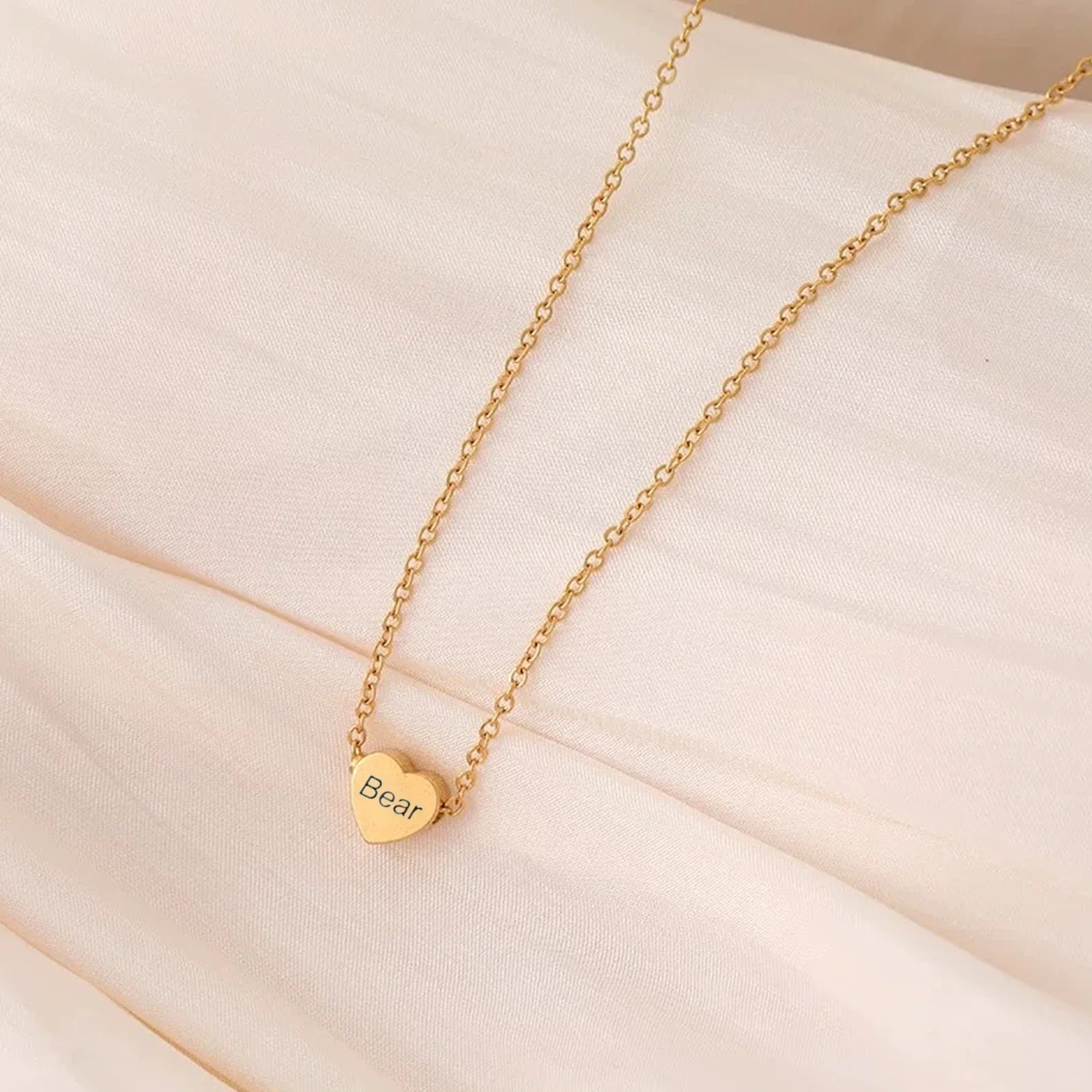 Gold necklace with a heart-shaped pendant on a beige fabric background