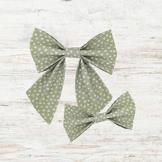 Two green patterned bows on a light wooden surface
