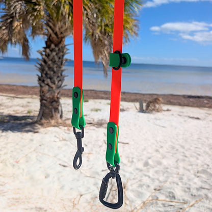 Bright orange and green multifunction dog leash with beach and palm tree in the background