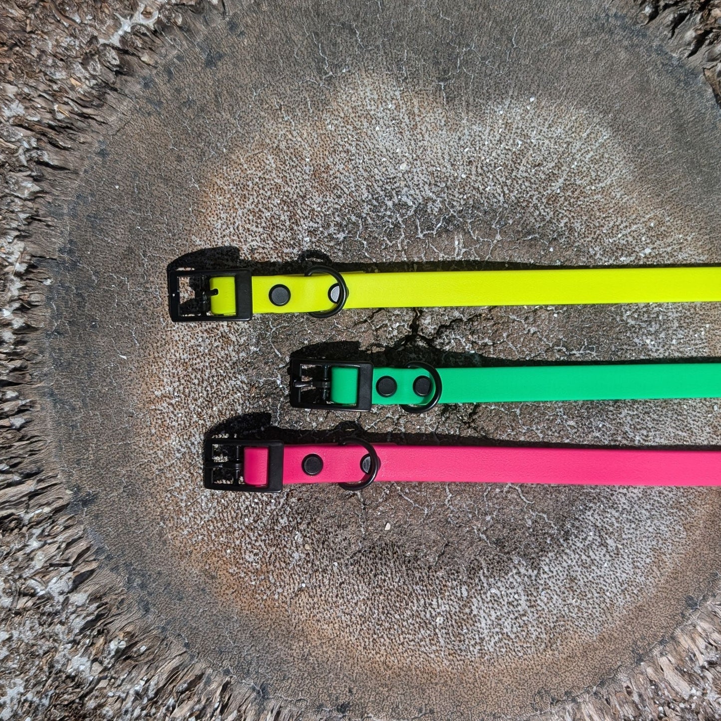 Three colorful dog collars (green, pink, and yellow) on a textured surface.