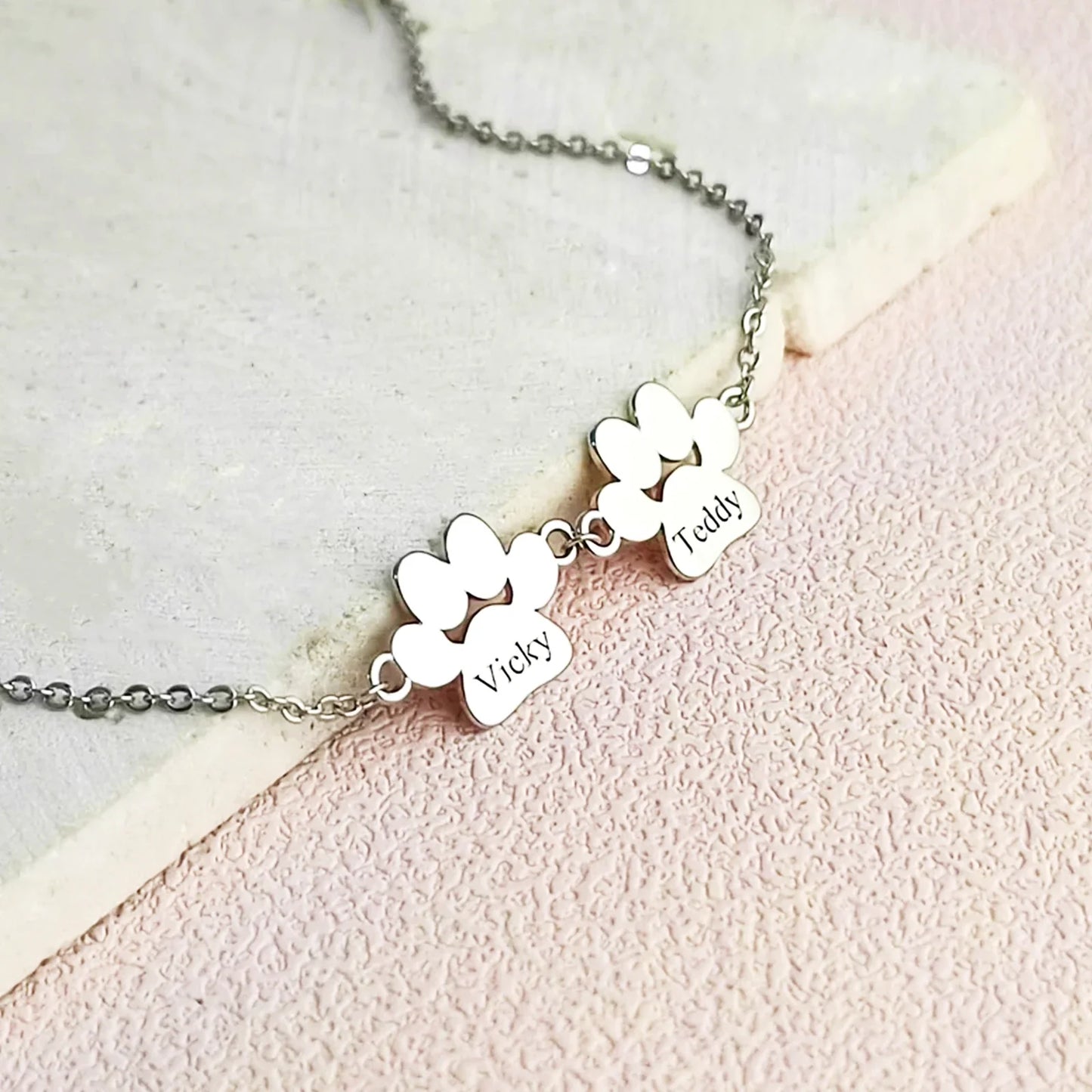 Silver bracelet with two engraved heart-shaped pendants on a light pink background