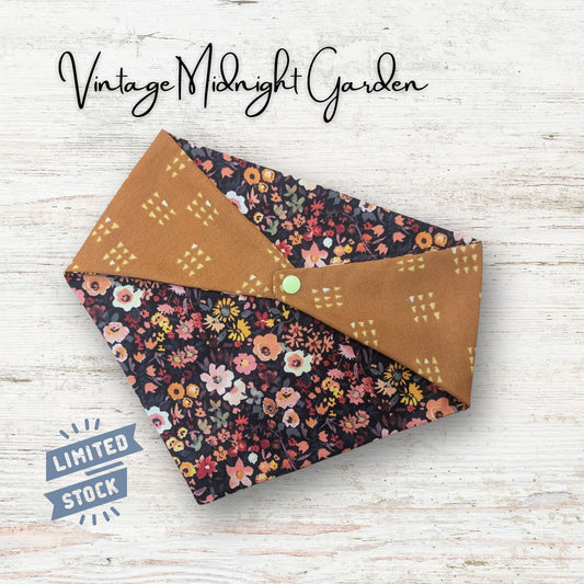 Reversible pet bandana featuring floral fabric with a rusty colored geometric pattern on a light wooden surface, featuring 'Vintage Midnight Garden' text